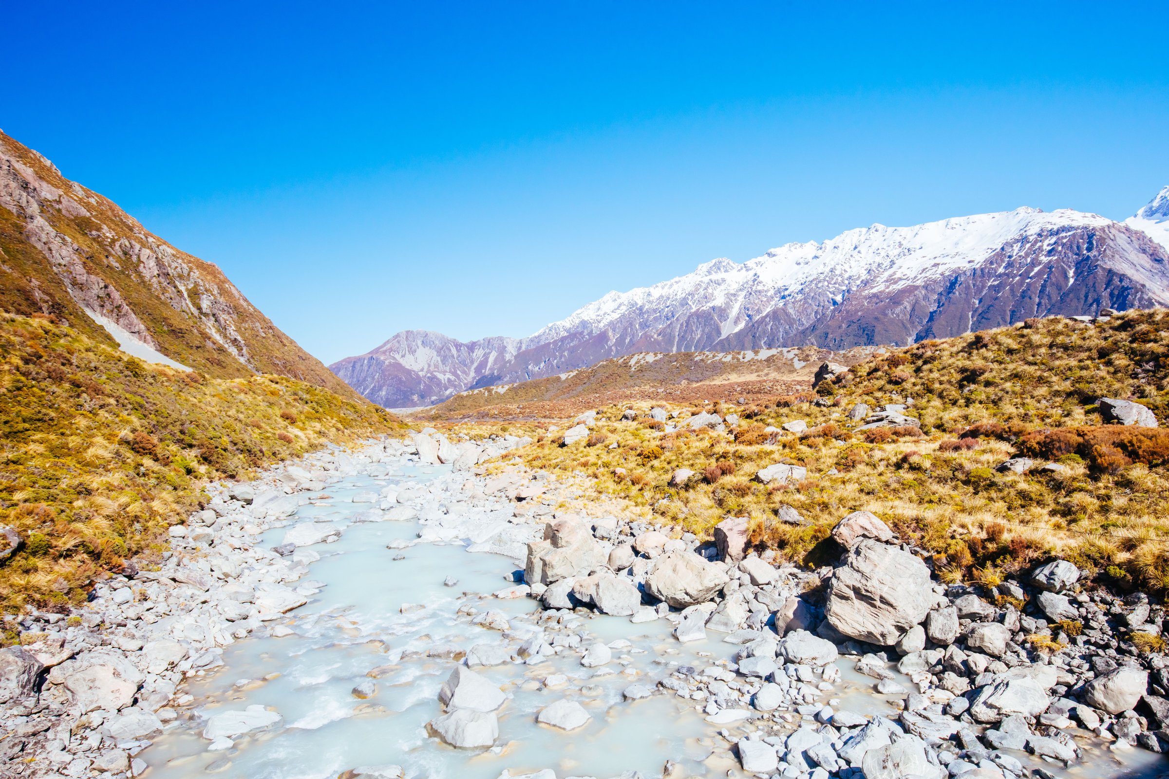 Sungai gletser berkelok mengalir dari pegunungan bersalju di Hooker Valley, Aoraki Mt Cook