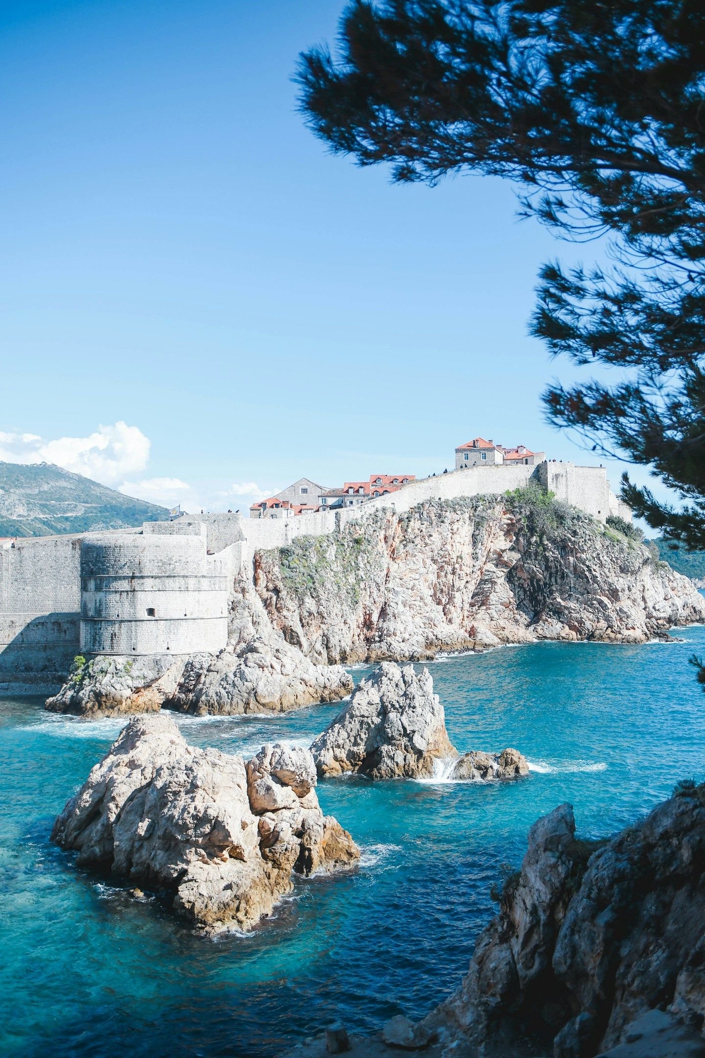 Tembok kota tua Dubrovnik di atas tebing karang dengan laut Adriatik biru toska di bawahnya