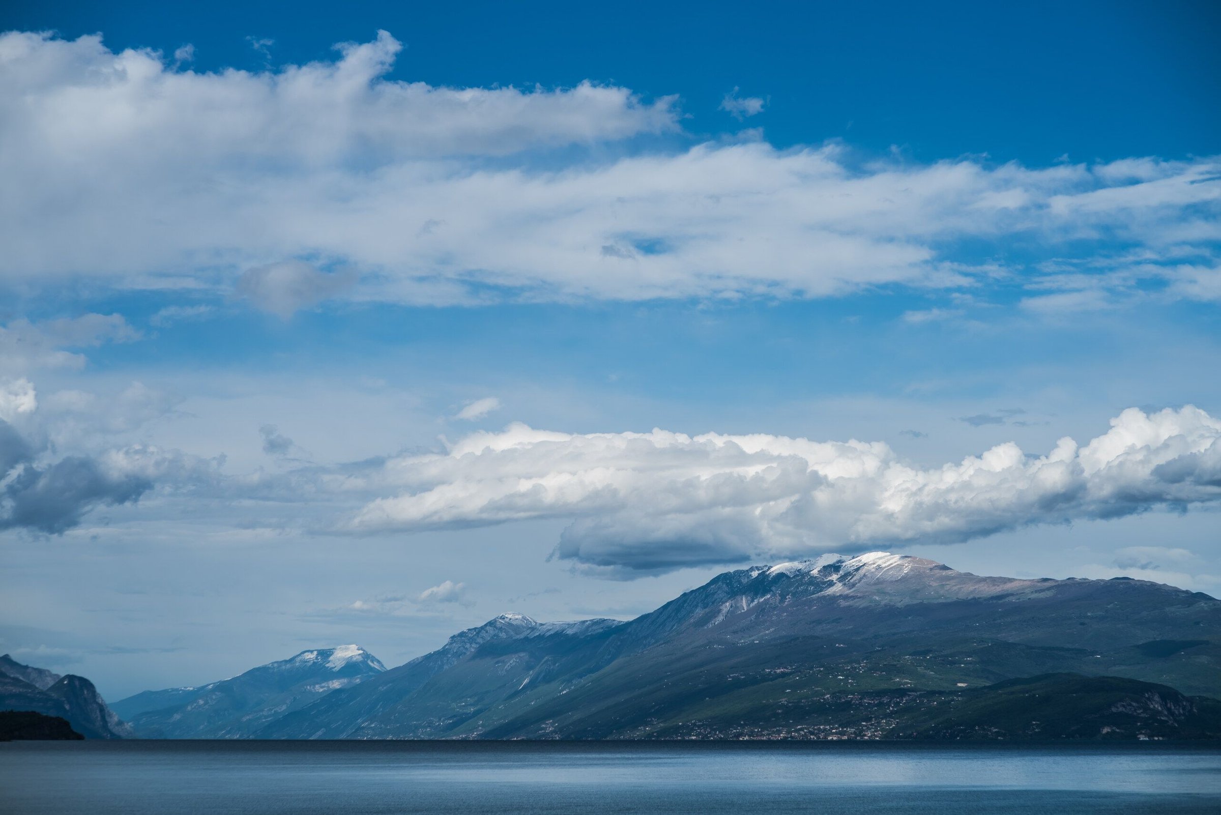 Lake Garda dengan pegunungan berpuncak salju di seberangnya di bawah langit berawan.