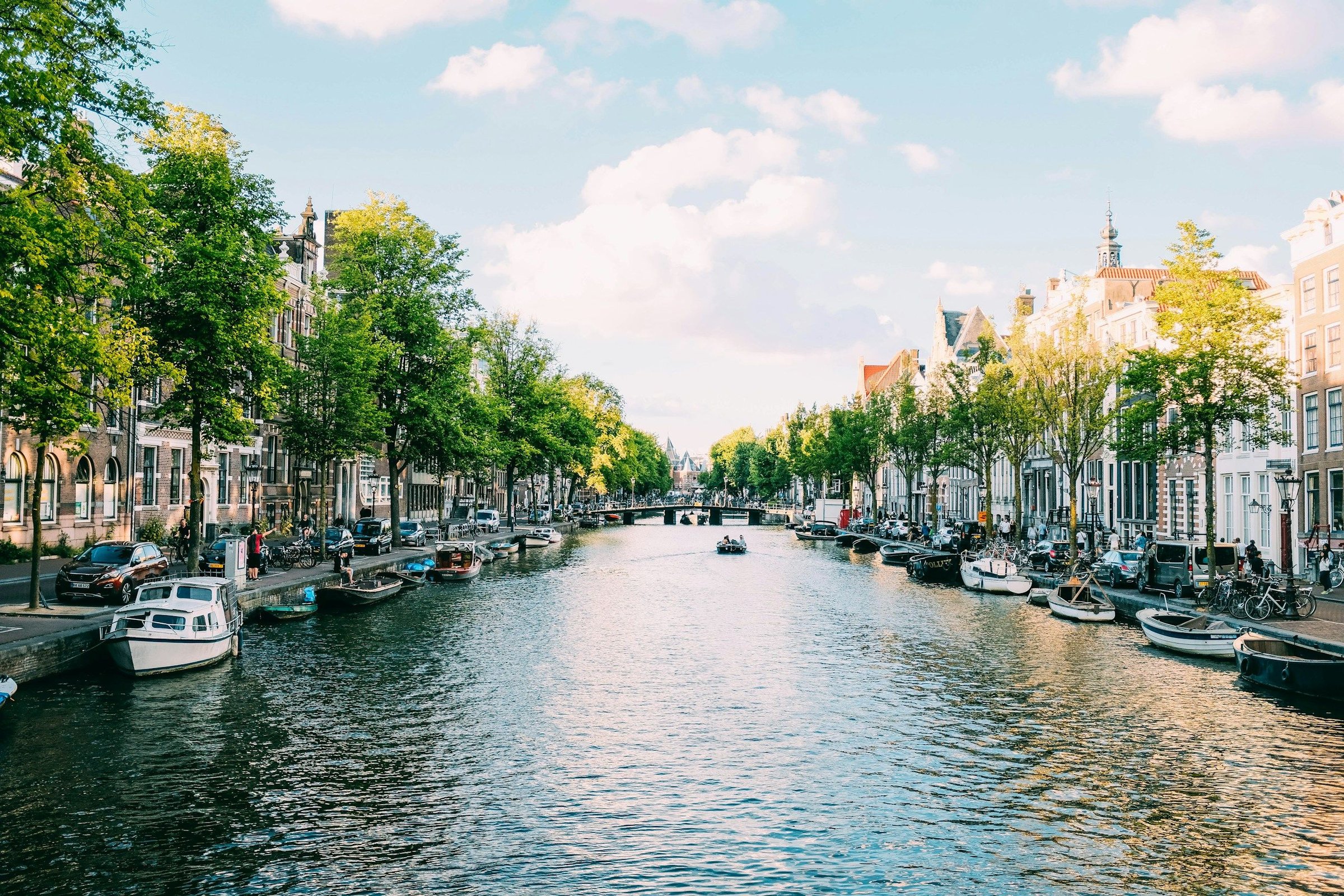 Kanal Amsterdam dikelilingi pepohonan hijau dan deretan rumah klasik Belanda