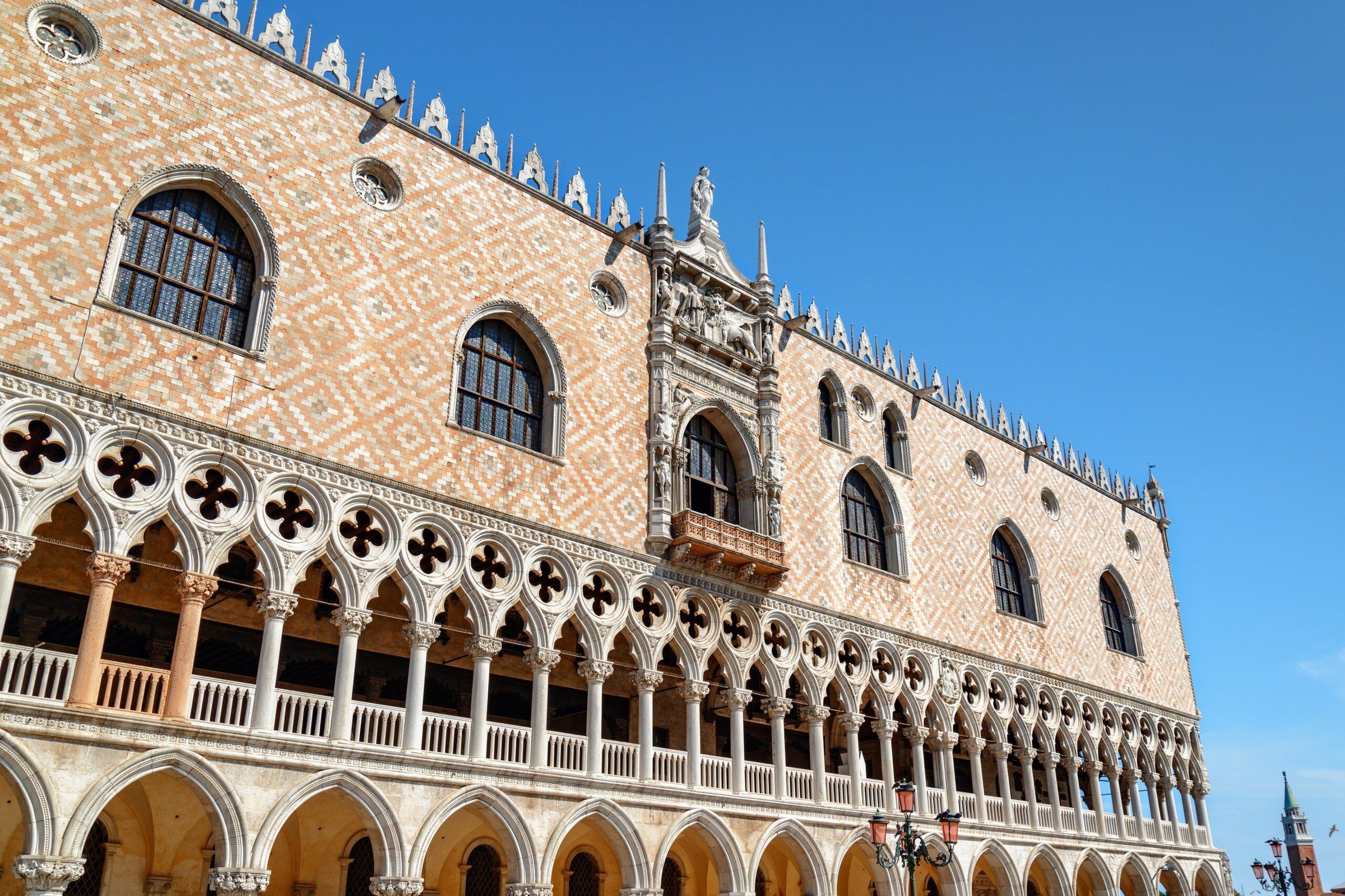 Fasad Doge's Palace di Venice dengan lengkung dan ornamen merah muda pucat di bawah langit biru.