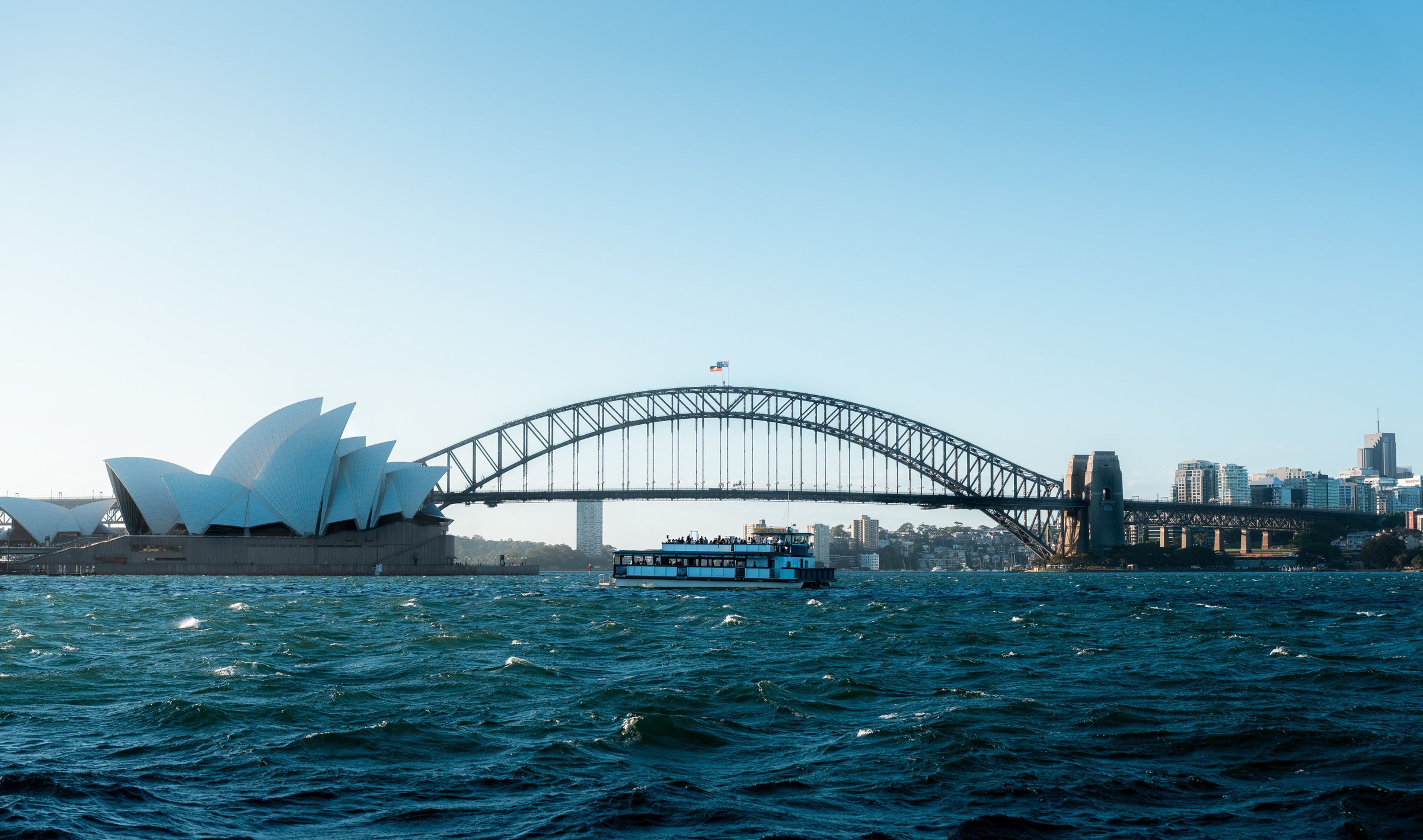 Kapal wisata melintas di depan Sydney Opera House dengan Harbour Bridge di langit cerah