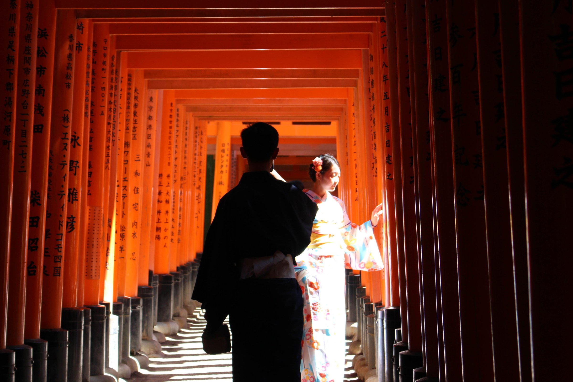 Pasangan berkimono berjalan di lorong torii merah Kuil Fushimi Inari, Kyoto