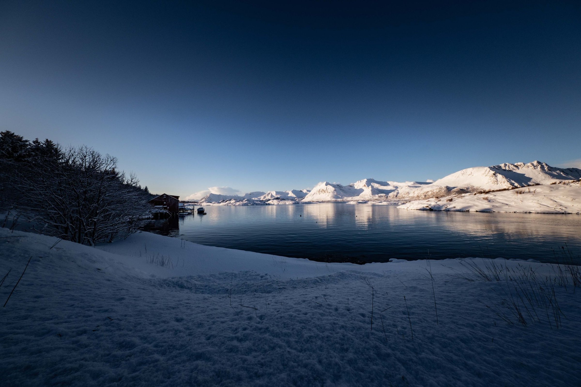 Pegunungan bersalju Lyngen Alps di seberang fjord biru, Norwegia utara.