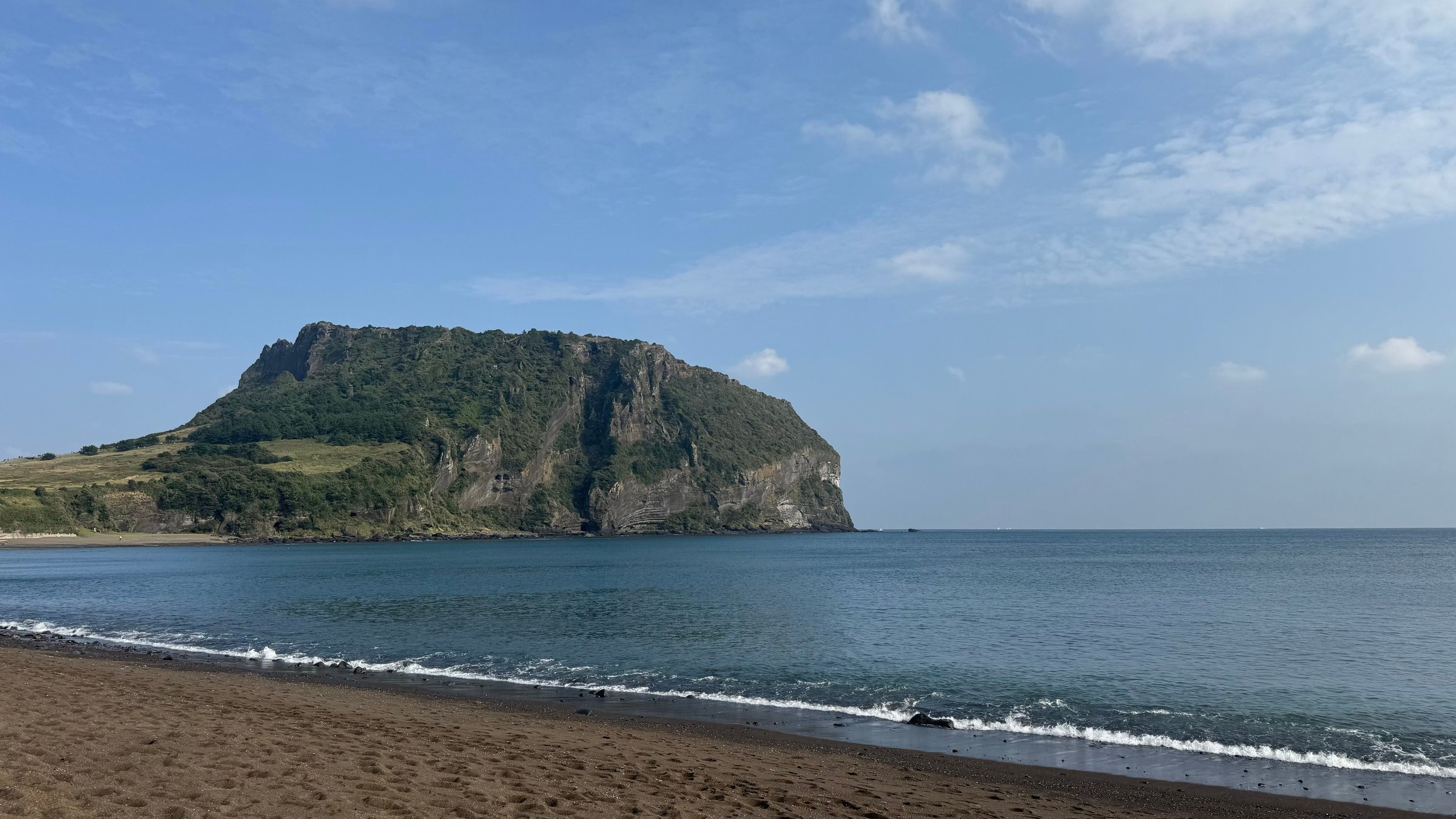 Kerucut vulkanik Seongsan Ilchulbong dilihat dari pantai berpasir gelap Jeju