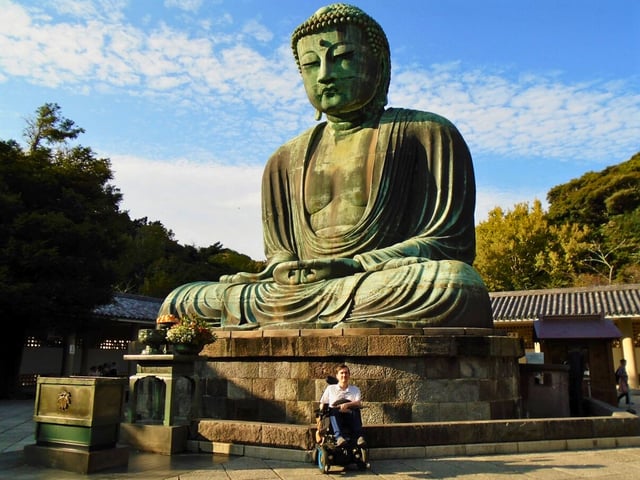 Justin in his power wheelchair sitting in front of the Giant Buddha of Kamakura on a sunny day