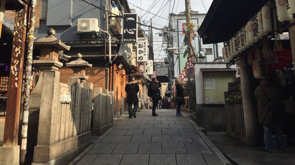 Hozenji Yokocho, A narrow street in Osaka, Japan, with traditional buildings, stone lanterns, and people walking and taking photos.
