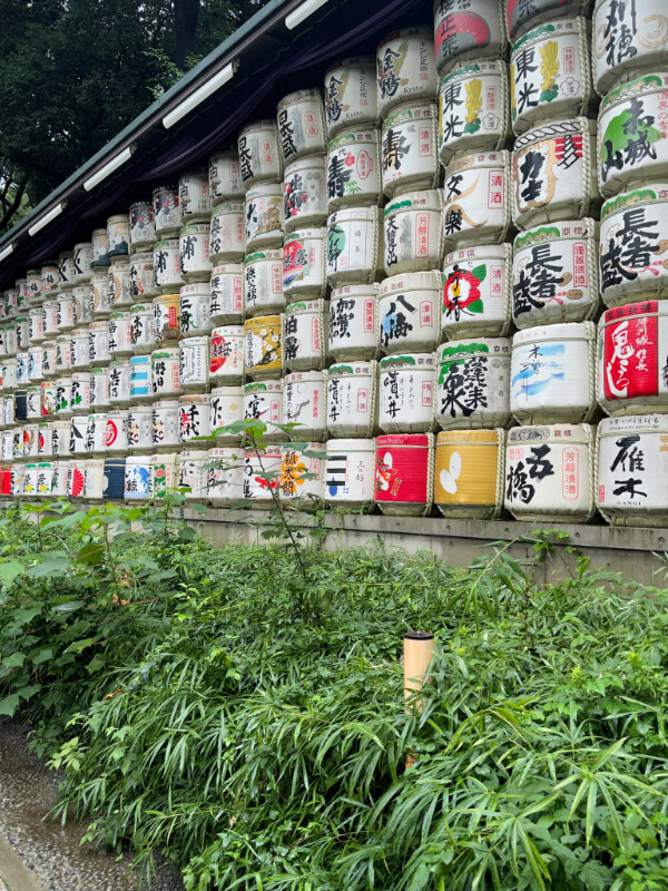 A vibrant display of colorful sake barrels stacked along a wall at Meiji Shrine in Tokyo. The barrels are donated by sake brewers as offerings, symbolizing the deep cultural traditions of Japan.