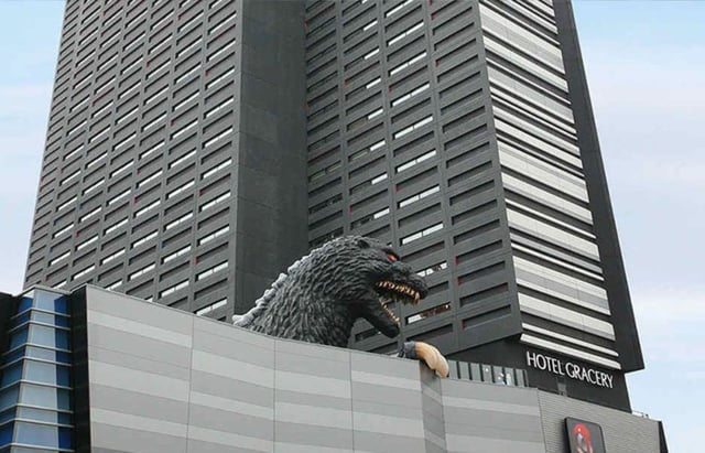 A giant Godzilla head peers over the top of Hotel Gracery in Shinjuku, Tokyo. The life-sized Godzilla replica adds a unique and iconic touch to the city’s skyline, drawing visitors' attention.
