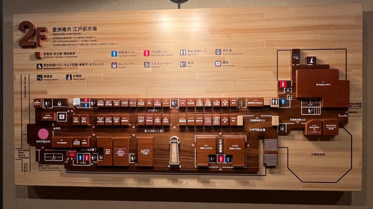 A wooden 3D map of Toyosu Edo-Mae Market's second floor. It highlights stores, restaurants, restrooms (including baby and multi-purpose), a smoking room, and a prayer room.