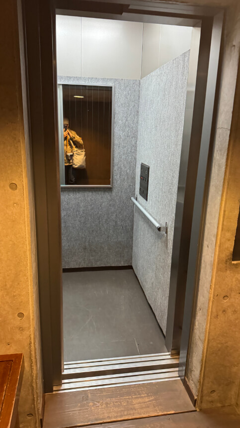 Small elevator with a handrail and mirror inside, lowered buttons for access by wheelchair users