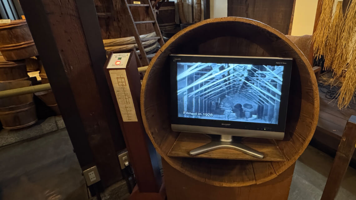 Video display in a wooden barrel showing a 1928 sake-making film. An English translation button is available for audio but not subtitles.