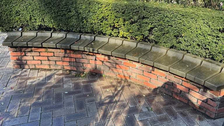 Curved brick bench, set beside trimmed hedges, offering a resting spot. Curved brick bench, set beside trimmed hedges, offering a resting spot.