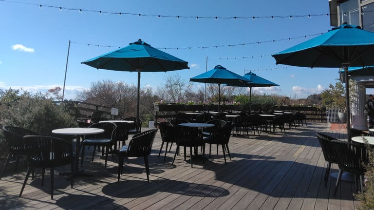 Outdoor rest area at the Glasshouse with tables, chairs, and blue umbrellas on a wooden deck. Outdoor rest area at the Glasshouse with tables, chairs, and blue umbrellas on a wooden deck.