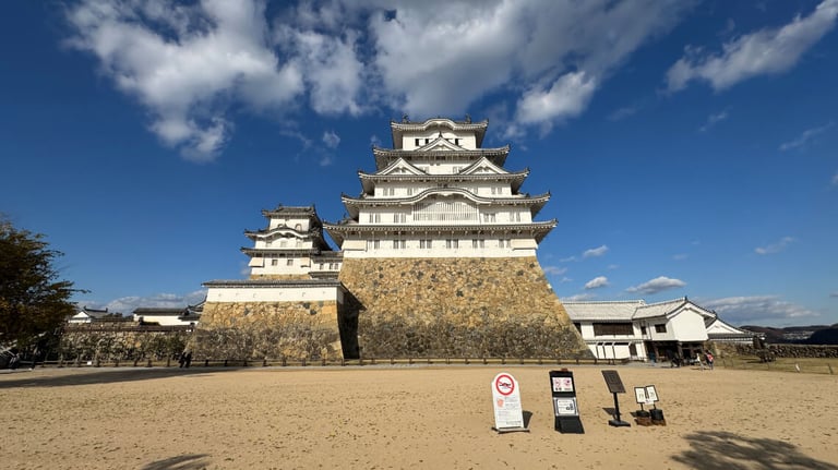 A view of the castle keep from Bizenmaru bailey, showcasing its towering white walls, stone base, and surrounding open courtyard. A view of the castle keep from Bizenmaru bailey, showcasing its towering white walls, stone base, and surrounding open courtyard.