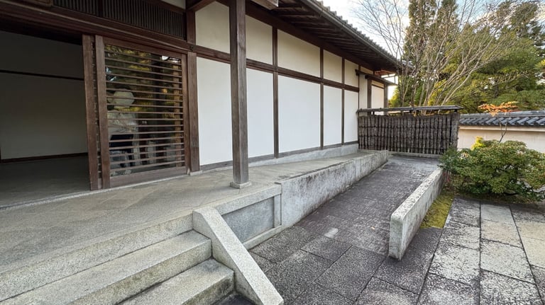 A traditional building with white walls and wooden frames, featuring both steps and a ramp for accessibility.