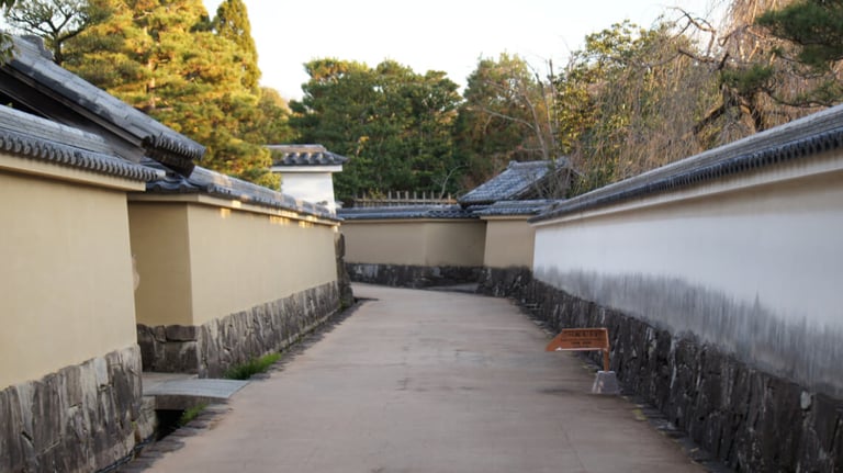 A narrow pathway bordered by yellow and white plaster walls with tiled roofs, leading through a walled section of the garden route.