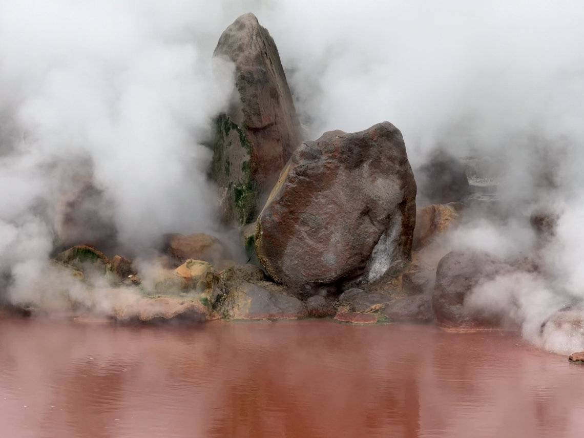 Steam rises around large rocks at Umi Jigoku, a red-hued hot spring in Beppu's famous geothermal area.