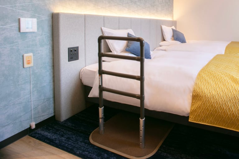 Twin bed with a bedside assist rail, wall-mounted controls, and a soft blue accent wall in an accessible room.