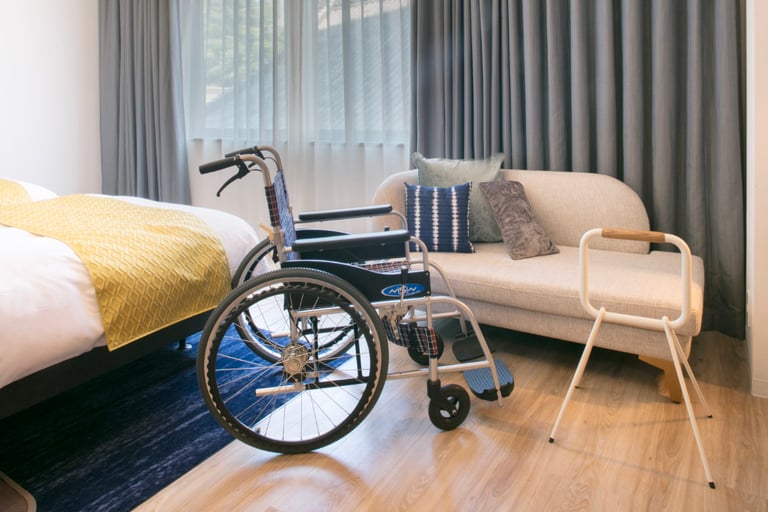 Accessible room setup with a wheelchair, assist rail near the sofa, and a bed with yellow bedding.