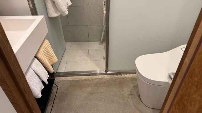 Compact bathroom with a sink and towels on the left, a modern toilet on the right, and a lip into a tiled shower area.