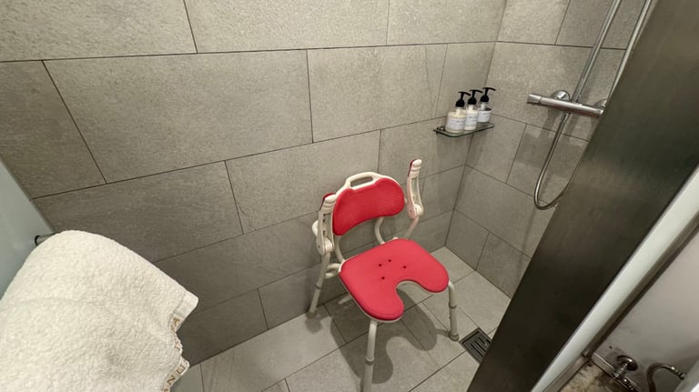 Accessible walk-in shower with gray tiles, a red and white shower chair, handheld showerhead, and wall-mounted toiletries.