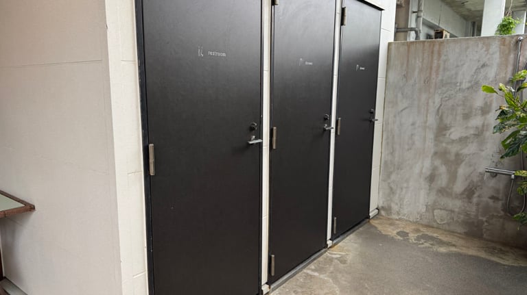 Three black doors labeled restroom and shower, set against an exterior wall with a nearby outdoor faucet.