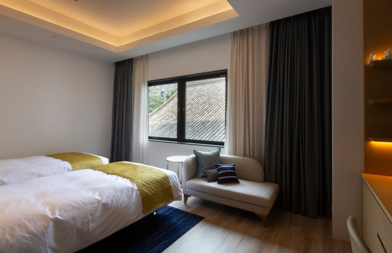 Accessible hotel room with two beds, wood flooring, a cushioned bench by the window, and soft ceiling lighting.