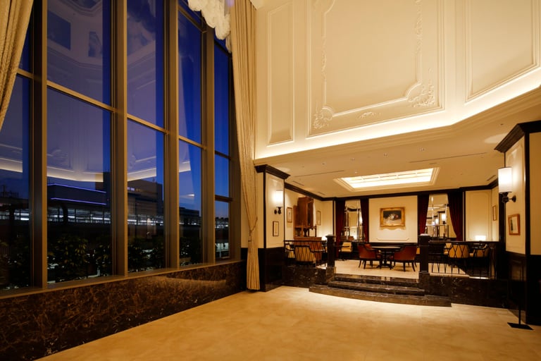 Elegant hotel lounge with high ceilings, marble floors, large windows, and classic-style furniture at night.