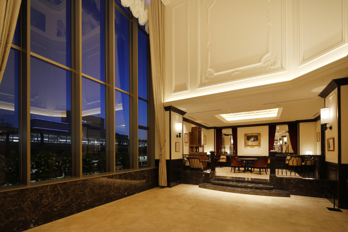 Elegant hotel lounge with high ceilings, marble floors, large windows, and classic-style furniture at night.