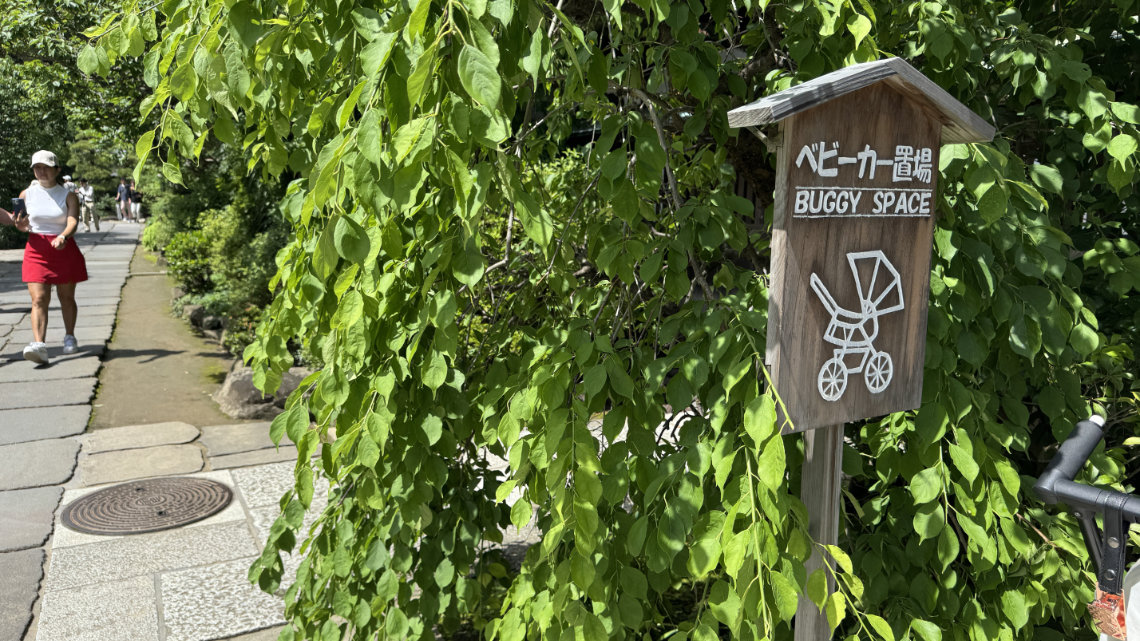 A sign reading “Buggy Space” with a stroller icon stands by a paved path shaded by leafy trees.