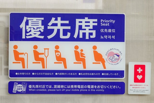 Japanese priority seat sign with icons showing elderly, injured, pregnant people, and a Help Mark symbol indicating support for people with invisible disabilities.