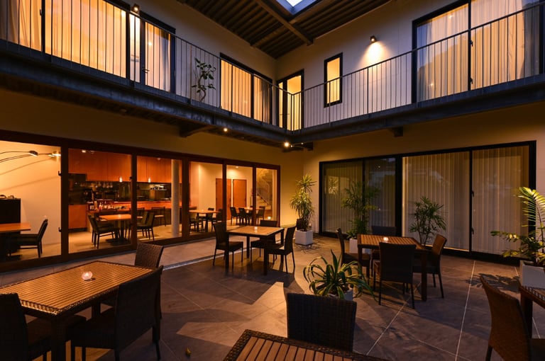 Courtyard at dusk with wicker tables, potted plants, and rooms overlooking from a second-floor balcony.