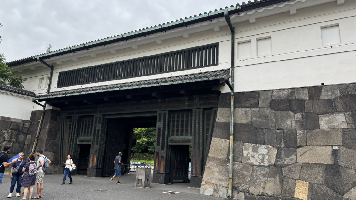 Visitors gather near the main gate of the Tokyo Imperial Palace, featuring stone walls and traditional Japanese architecture.