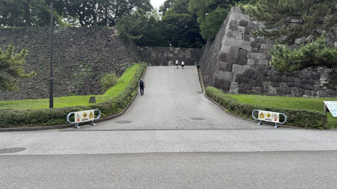 Steep slope between stone walls at the Imperial Palace with warning signs for wheelchair users at the entrance.