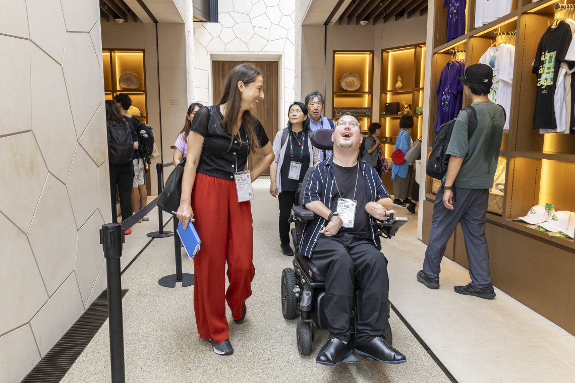 A man in a wheelchair and a woman share a laugh while exploring the Saudi Arabia Pavilion’s gift shop at Expo 2025.
