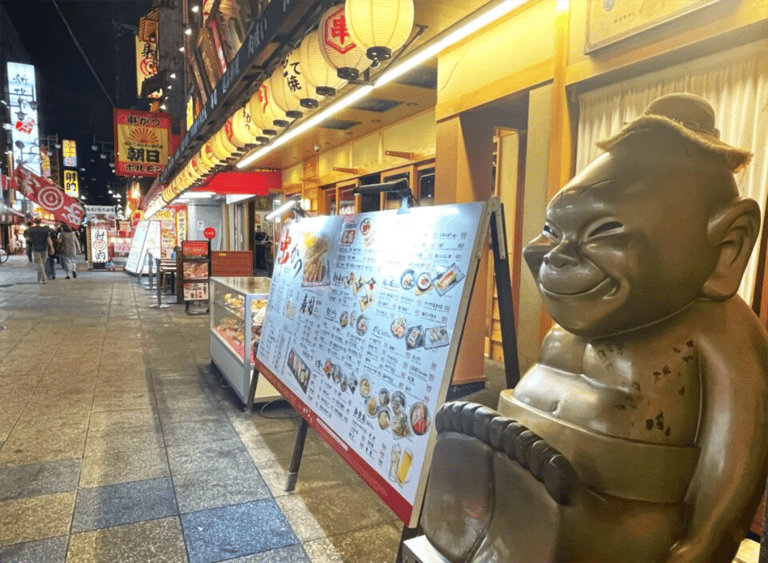 accessible osaka shinsekai evening tour billiken statue and menu boards at night 768x564