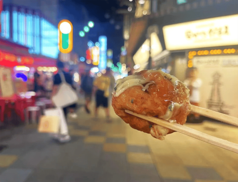 accessible osaka shinsekai evening tour takoyaki closeup with neon bokeh 768x588