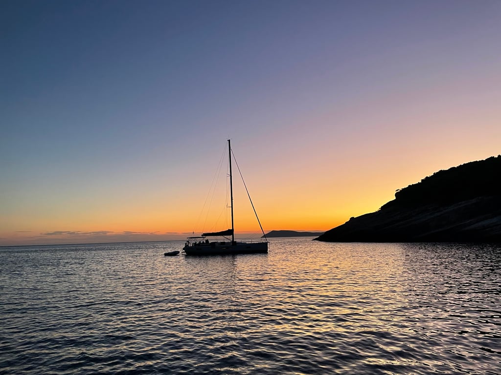Turquoise bay in Vis with our sailboat at anchor near the rocky shoreline