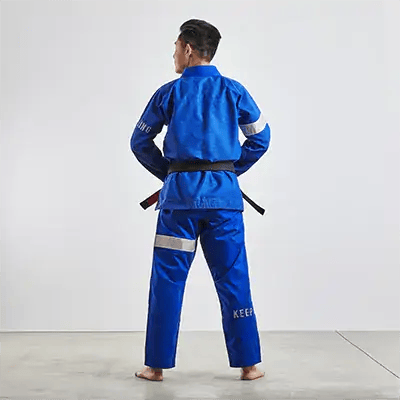 มุมมองด้านหลังของบุคคลที่สวมชุด BJJ gi สีน้ำเงินที่มีตรา 'KING' ที่ด้านหลัง ผูกด้วยเข็มขัดสีดำ