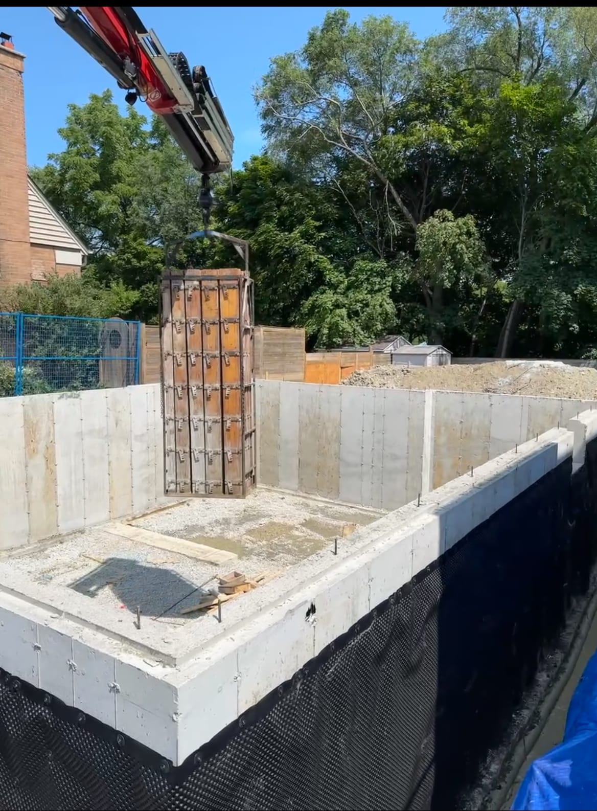 Waterproofed residential foundation in Etobicoke ready for backfill with crane removing formwork systems