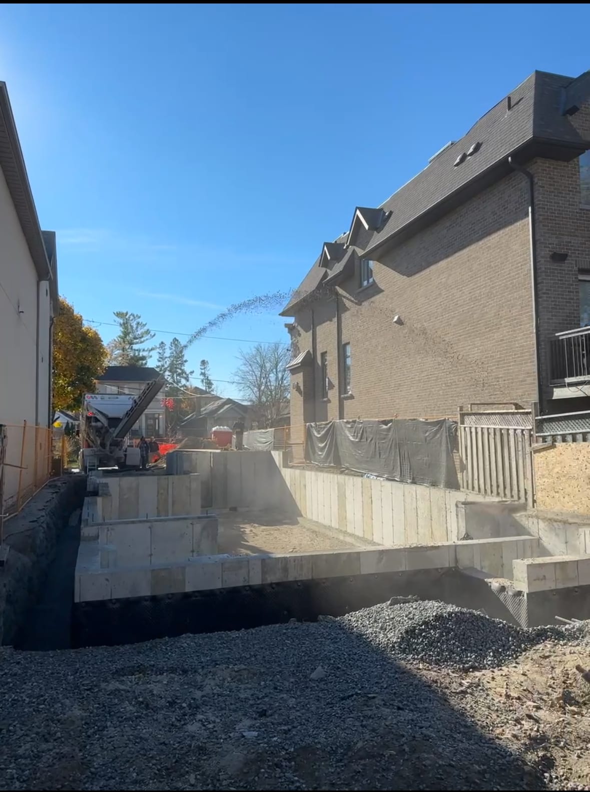 Stone slinger distributing drainage gravel around completed foundation walls in North York