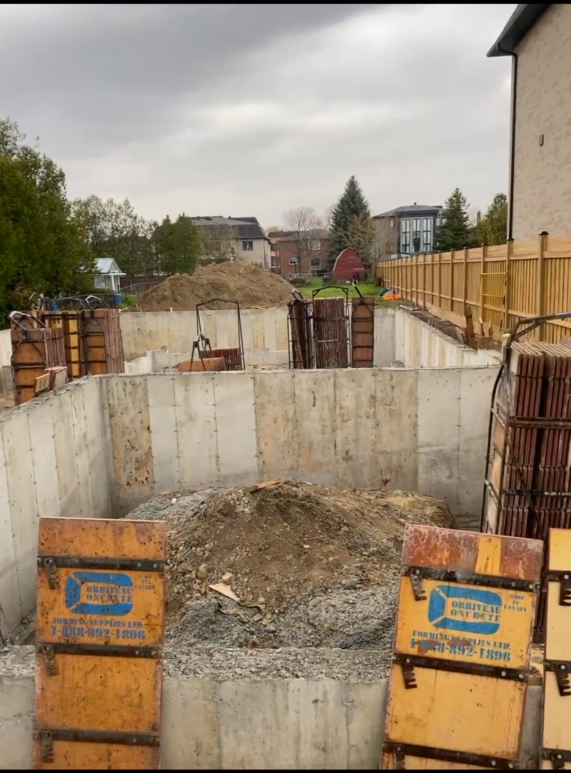Waterproofing application on stripped Scarborough foundation walls with reinforcement cages staged nearby