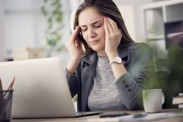 Woman with headache researching injury claim on laptop