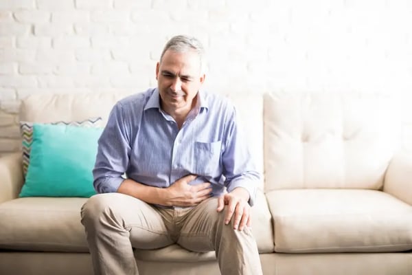 Injured man sitting on sofa holding a pain in his stomach