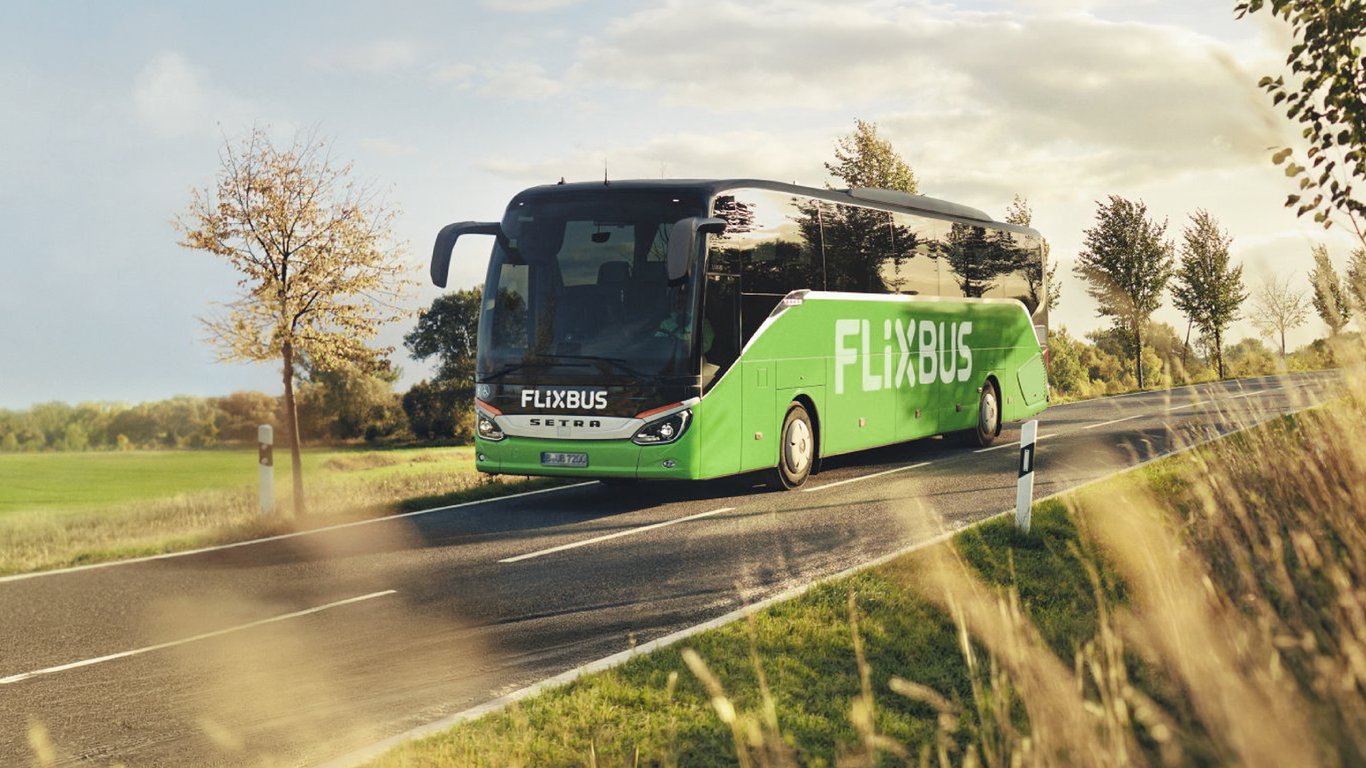 A green FlixBus coach driving on a tree-lined country road, one of around 1,700 Flix vehicles running passenger Wi-Fi with Peplink.