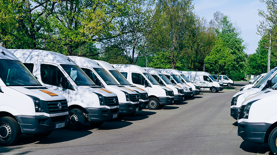 Rows of white fleet vans parked in a lot.
