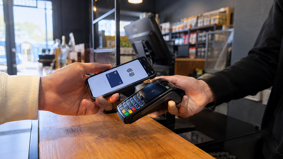 Customer making a contactless payment at a retail counter using a smartphone and card reader.