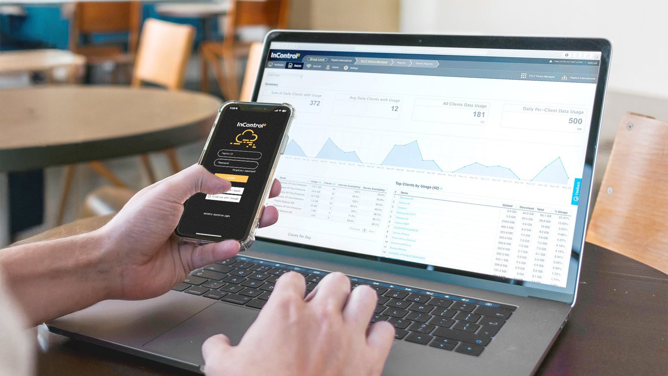 Person monitoring Peplink network performance on InControl 2 across a laptop and mobile device.