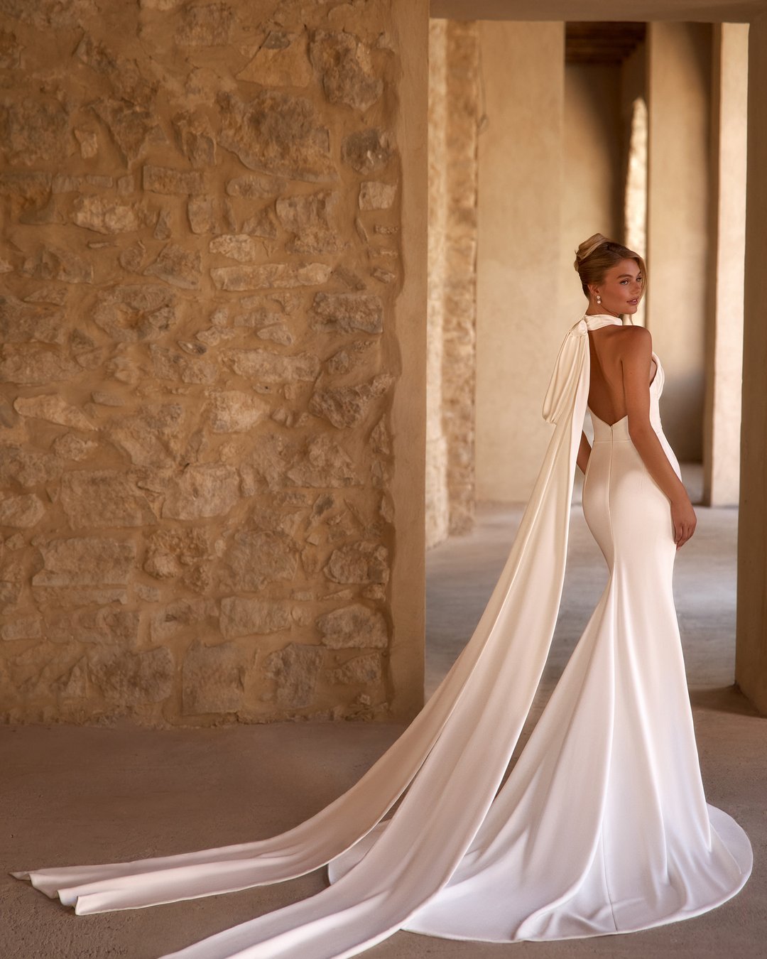 Suknia ślubna Fokuella z kolekcji AnnaSposa to kwintesencja elegancji i klasyki, która zachwyca lekkością i perfekcyjnym dopasowaniem. Jej gładka satyna oraz dekolt halter podkreślają sylwetkę, a wycięte plecy i marszczenia w talii dodają wyjątkowego uroku. Odpinana kokarda oraz tren sprawiają, że każda panna młoda poczuje się niczym prawdziwa księżniczka w tym niezwykłym modelu.